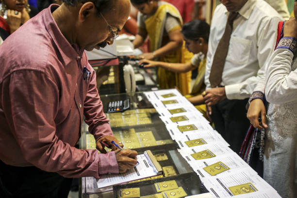 An employee writes on a counter as customers browse gold coins inside a Titan Co. Tanishq jewelry store during the festival of Dhanteras in Mumbai, India, on Friday, Oct. 25, 2019. Gold sales on the most auspicious day in India to buy the metal tumbled this year as high prices and concerns about an economic slowdown saw customers limit purchases. Photographer: Dhiraj Singh/Bloomberg via Getty Images